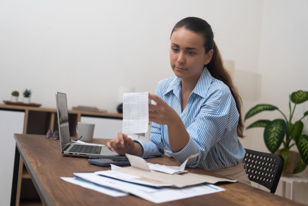 Young lady sits at table calculating utility payments before make money transfer in online bank app