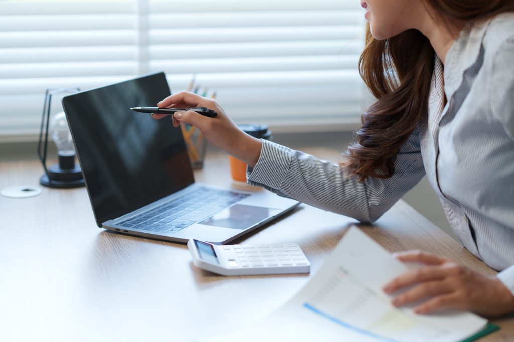 Businesswoman analyzing data on laptop and calculating tax with calculator in office